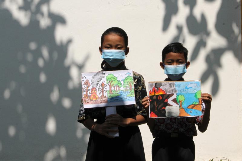 Murid sekolah dasar (SD) terlihat mengenakan masker dan memegang poster bertema kampanye stop kebakaran hutan dan lahan (karhutla) yang mereka gambar menggunakan krayon dan pensil warna di SDN Nayu Barat 1, Nusukan, Surakarta, Provinsi Jawa Tengah, pada 21 Oktober 2026. (Xinhua)
